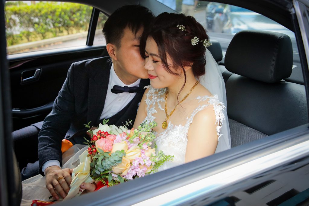 Bride and groom intimate moment in wedding car with bouquet Singapore