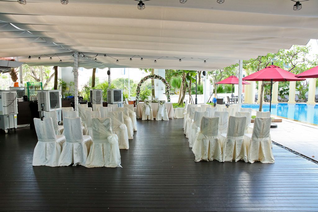Outdoor poolside wedding ceremony setup with white chairs and floral arch Singapore