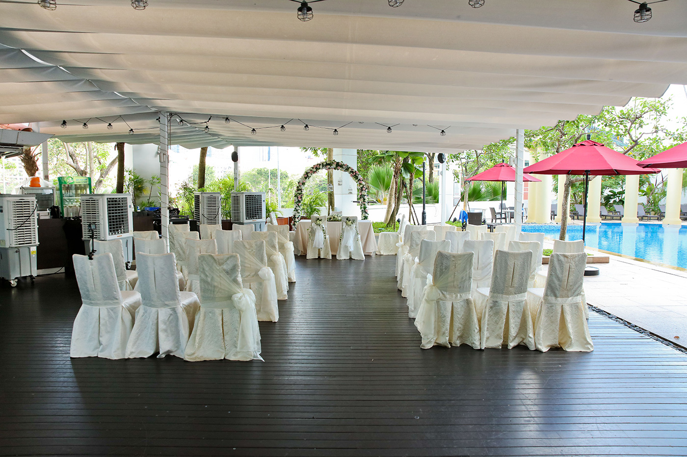 Outdoor poolside wedding ceremony setup with white chairs and floral arch Singapore
