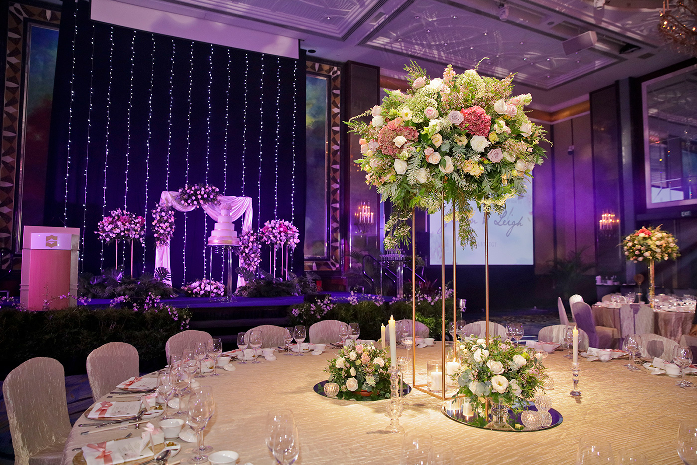 Elegant purple wedding reception stage with tall floral centerpieces and crystal decor