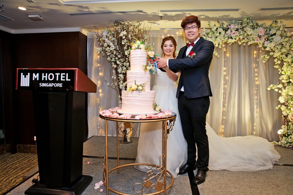 Wedding cake cutting ceremony at M Hotel Singapore with elegant floral backdrop