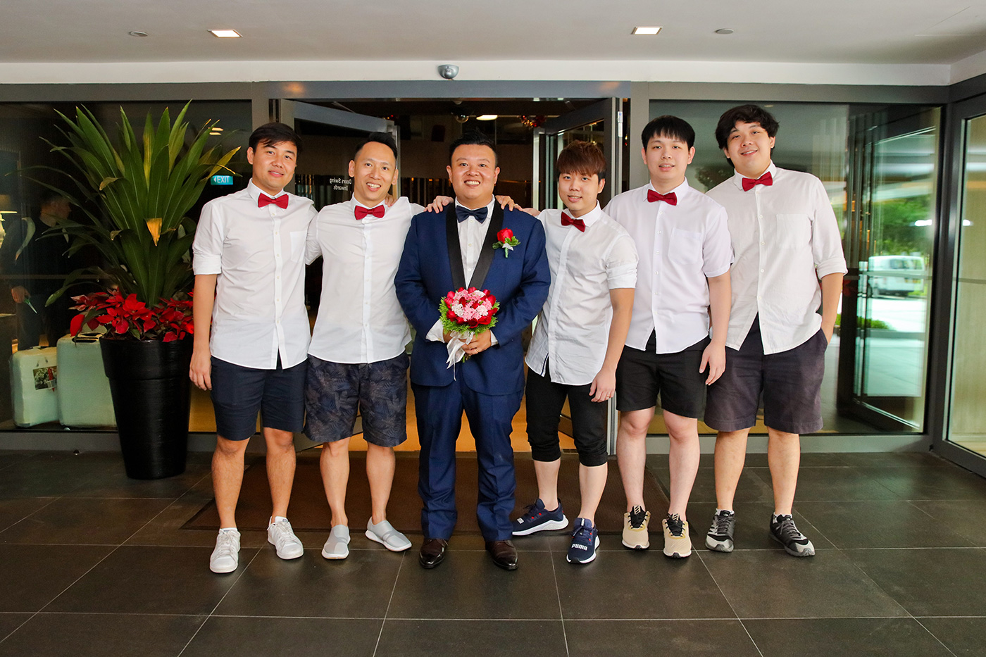 Groomsmen in white shirts and red bow ties group photo with groom in navy suit
